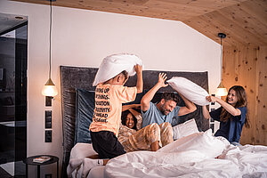 Familie hat eine Kissenschlacht im Bett im Luxushotel im Zillertal STOCK resort